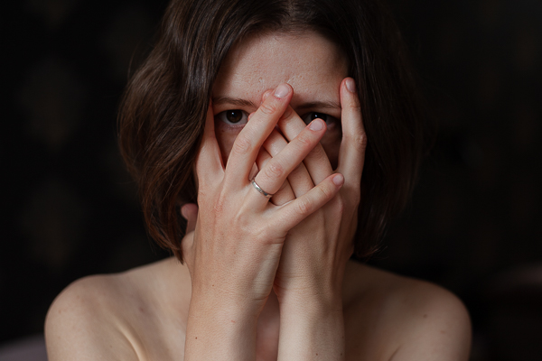 A portrait of a woman covering her face and looking through her fingers.