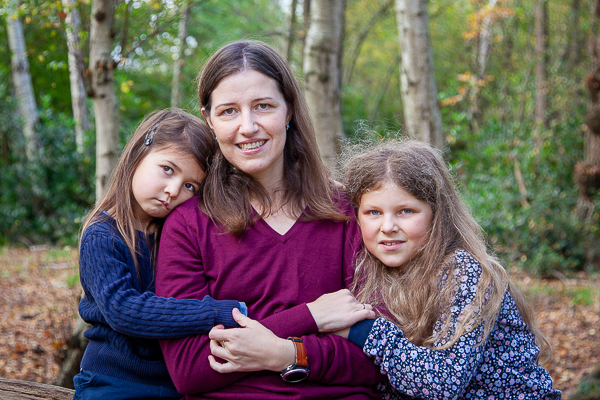 Family photograph of a mother sitting outdoors with her two children, holding them close.