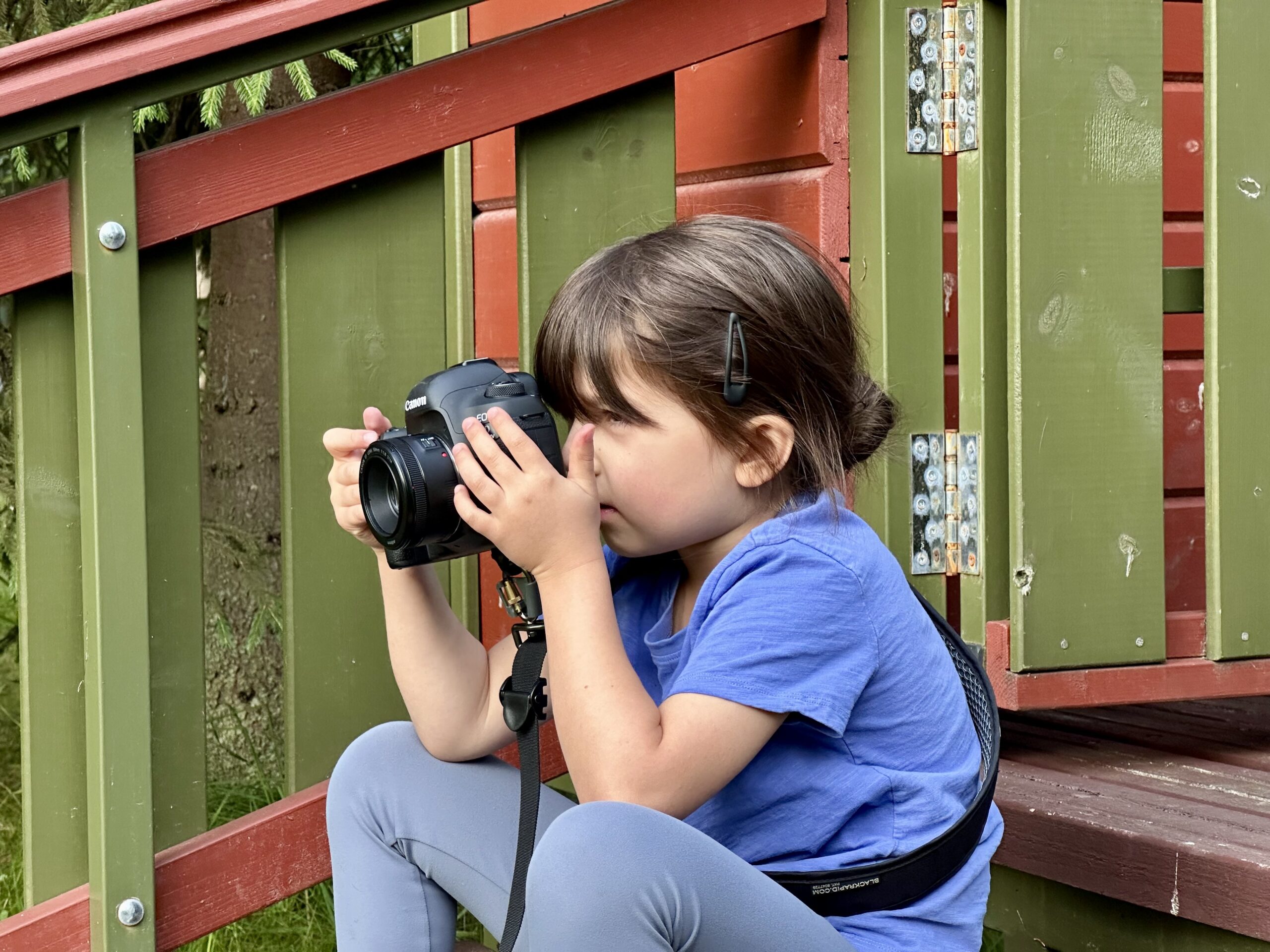 Young child sitting outdoors and taking a photo with a camera during a school holiday activity