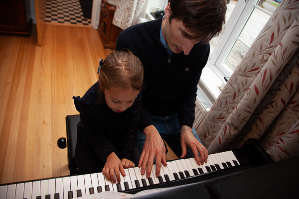 Father and young daughter sitting at a piano playing together indoors, candid family photography in Fleet, Hampshire