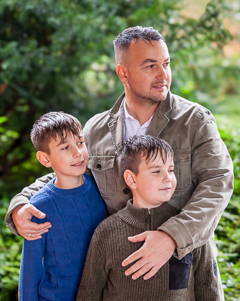 Father standing outdoors with two young boys, arms around them, natural family photography in Fleet, Hampshire.