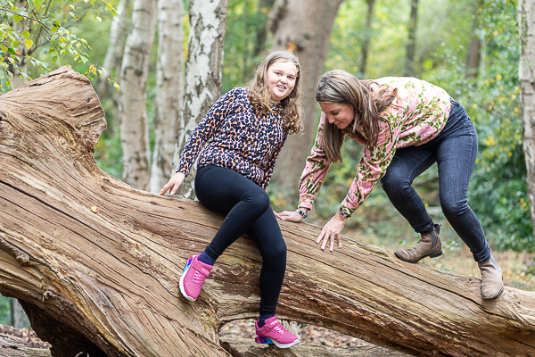 Mum and daughter climbing a fallen tree during a relaxed outdoor family photoshoot in Hampshire.